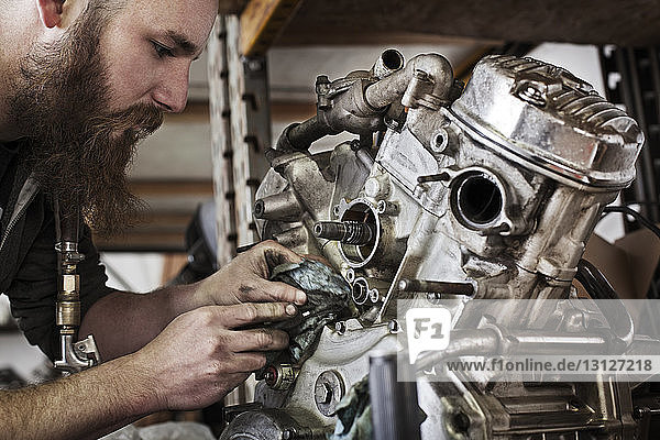 Beschnittenes Bild eines Mechanikers  der in der Werkstatt am Motorradmotor arbeitet
