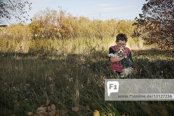 Junge trägt Hund  während er auf einem Grasfeld im Park sitzt