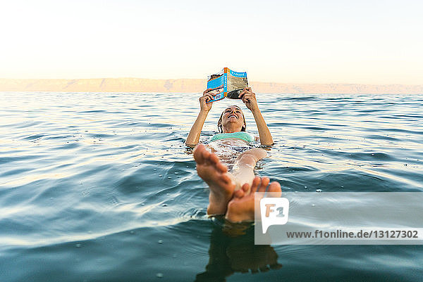Woman reading book while floating in sea