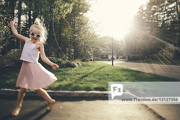 Smiling girl enjoying on street by grassy field during sunny day
