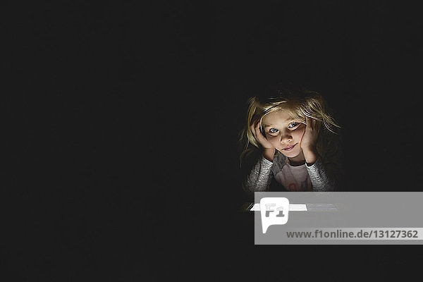 Gelangweiltes Mädchen benutzt digitales Tablett  während es zu Hause in der Dunkelkammer sitzt
