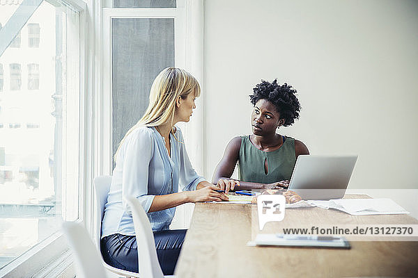 Young businesswomen discussing at conference table in creative office