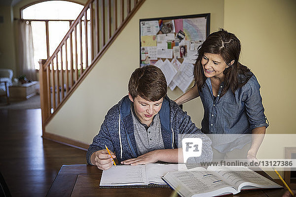 Lächelnde Mutter sieht Sohn beim Lernen auf dem Tisch an