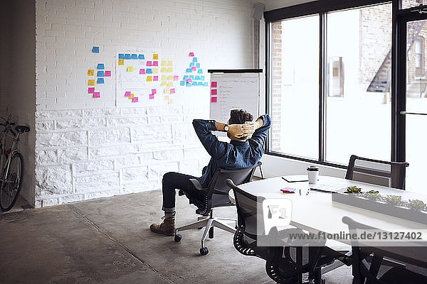 Geschäftsmann auf Stuhl sitzend mit Händen hinter dem Kopf im Kreativbüro