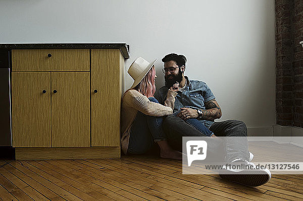 Glückliches Paar  das zu Hause auf dem Boden an der Wand sitzt