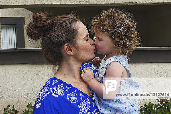 Nahaufnahme einer glücklichen Mutter  die ihre Tochter küsst  während sie an einer Mauer im Hof steht