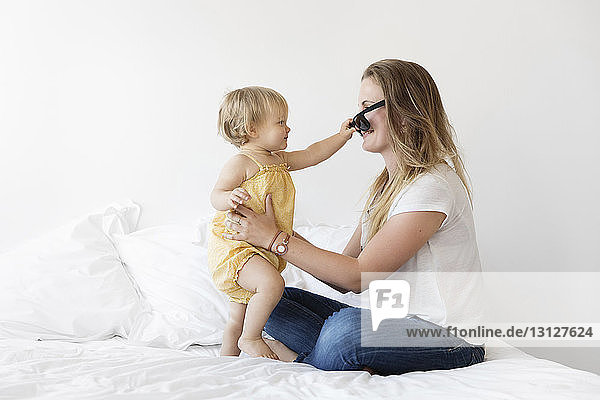 Seitenansicht einer Mutter  die mit ihrer Tochter spielt  während sie zu Hause im Bett sitzt