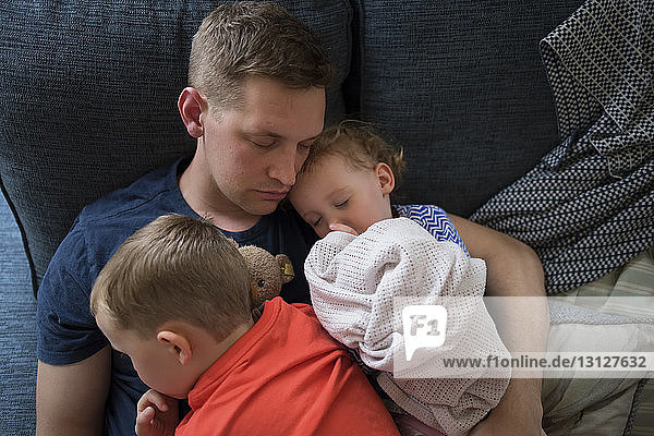 Hochwinkelaufnahme eines Vaters mit Kindern  die zu Hause auf dem Sofa schlafen