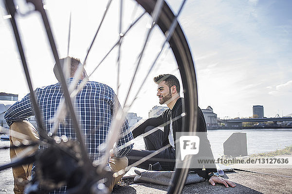 Freunde sitzen mit dem Fahrrad vor dem Kanal vor klarem Himmel