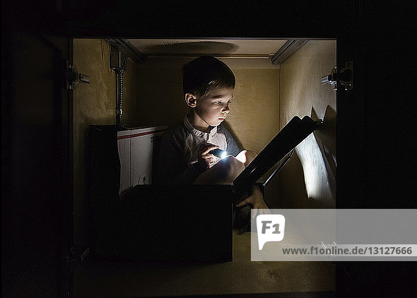 Boy hiding in cabinet and reading at home