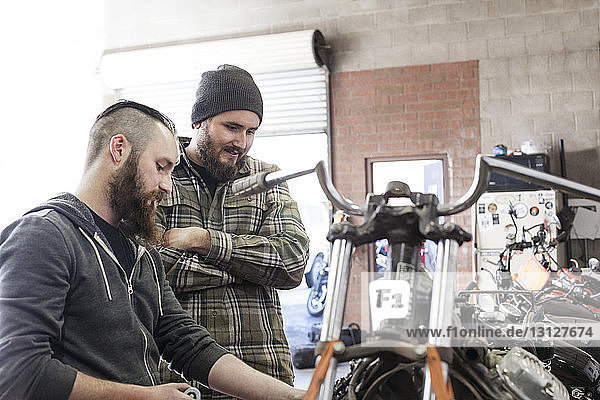Mann schaut auf Mechaniker  der in einer Autowerkstatt am Motorrad arbeitet