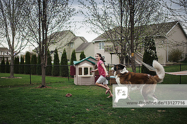 Fröhliches Mädchen spielt mit Hund auf Grasfeld im Hof