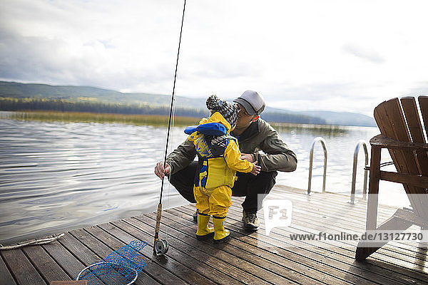 Father holding fishing rod while kissing son on wooden pier over lake