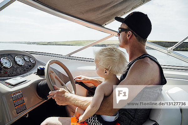 Seitenansicht eines Vaters mit Sohn am Steuer eines Motorbootes