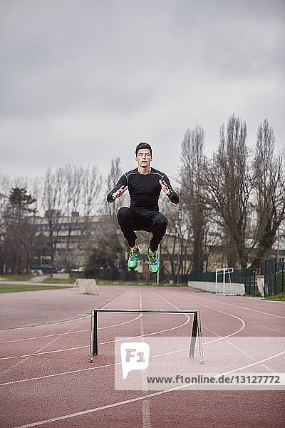 Porträt eines männlichen Athleten  der auf einer Sportbahn vor bewölktem Himmel trainiert
