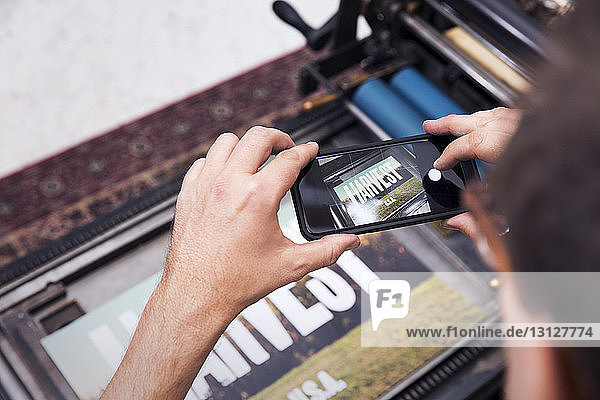 Cropped image of man photographing printed poster with smart phone