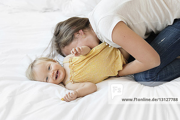 Hochwinkelaufnahme einer glücklichen Mutter  die ihre Tochter zu Hause im Bett kitzelt