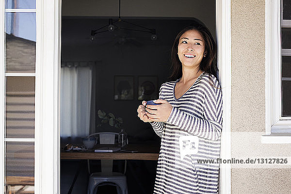 Nachdenkliche Frau hält Kaffeetasse  während sie an der Tür steht