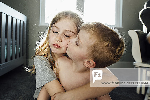 Junge ohne Hemd küsst Schwester zu Hause