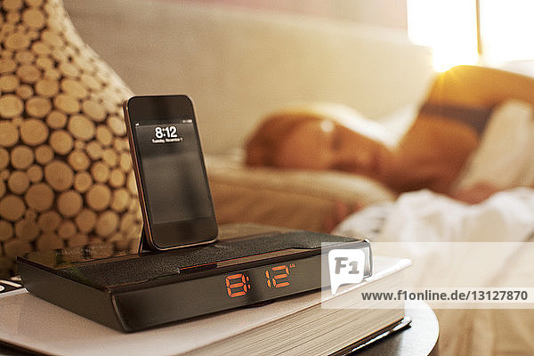 Smart phone on modern alarm clock in bedroom