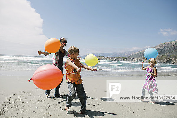 Happy family playing with balloons while standing on sand at beach
