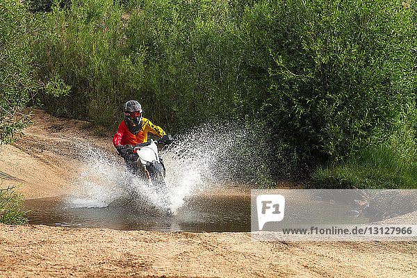 Man riding dirt bike and splashing water in puddle