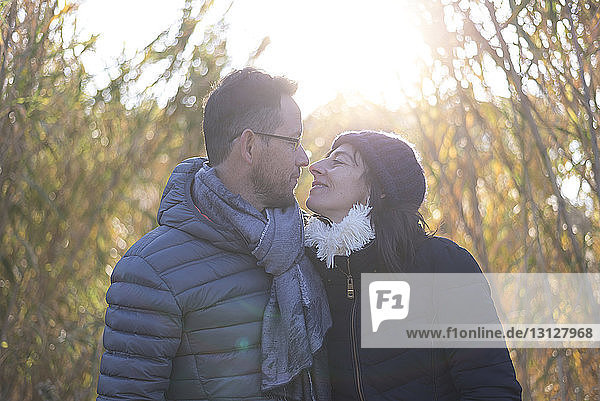 Loving mature couple wearing warm clothing while looking each other on field during sunny day