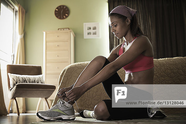 Woman putting on sports shoe while sitting at home