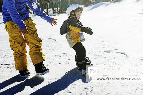 Hochwinkelansicht des Vaters  der der Tochter beim Snowboarden hilft