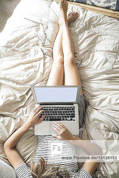 High angle view of woman using laptop computer while lying on bed