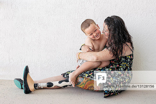 Mutter mit Beinprothese umarmt Sohn  während sie an der Wand sitzt