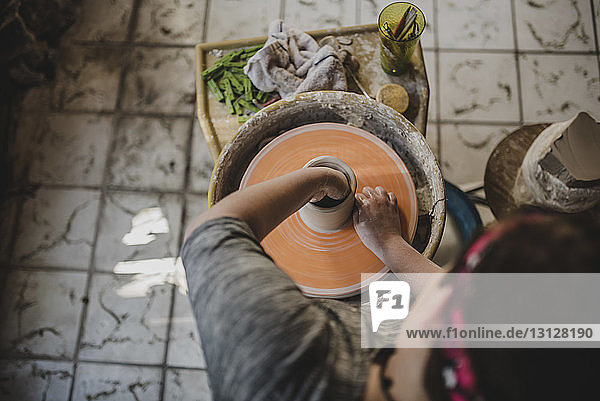 High angle view of potter using pottery wheel to make clay pot at workshop