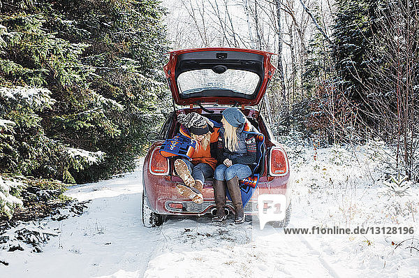 Freundinnen sitzen im Winter im Kofferraum eines Autos im Algonquin-Provinzpark