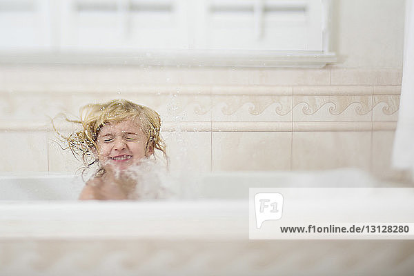 Girl with eyes closed splashing water while bathing in bathtub at home