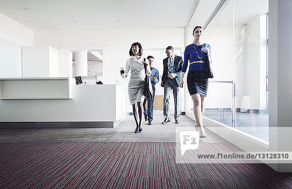Business people walking on corridor by glass in office