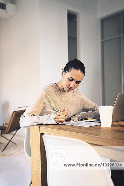 Geschäftsfrau schreibt  während sie im Büro am Schreibtisch sitzt