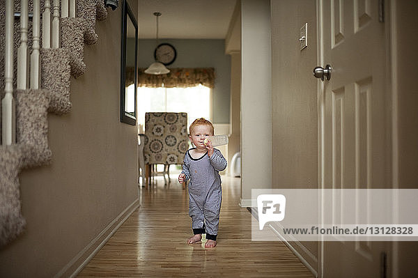 Porträt eines süßen Jungen  der Milch aus der Flasche trinkt  während er zu Hause auf dem Boden steht