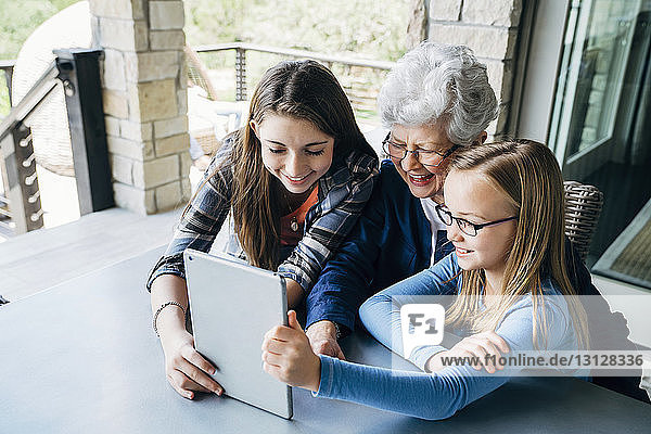 Hochwinkelansicht von Enkelinnen mit Tablet-Computer mit Großmutter auf der Veranda