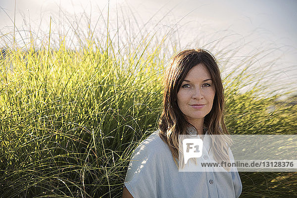 Portrait of beautiful woman standing against grass on sunny day