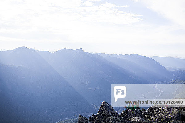 Hochwinkelaufnahme einer Frau  die auf Felsen sitzend vor einer Bergkette fotografiert
