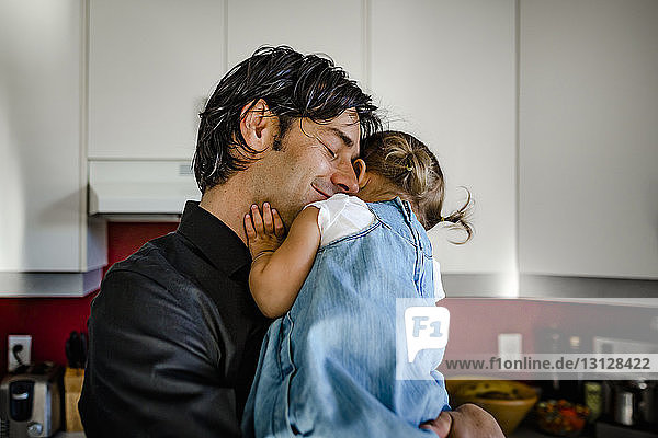 Lächelnder Vater umarmt Tochter  während er sie zu Hause in der Küche trägt