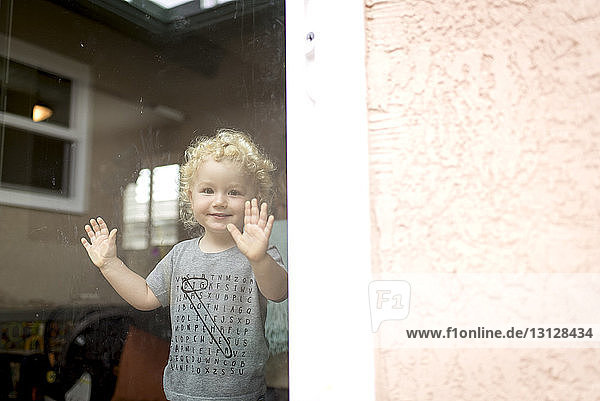 Porträt eines süßen Jungen  der zu Hause steht und durch ein Fenster gesehen wird