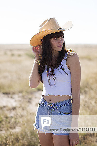 Frau mit Cowboyhut schaut weg  während sie auf dem Feld steht