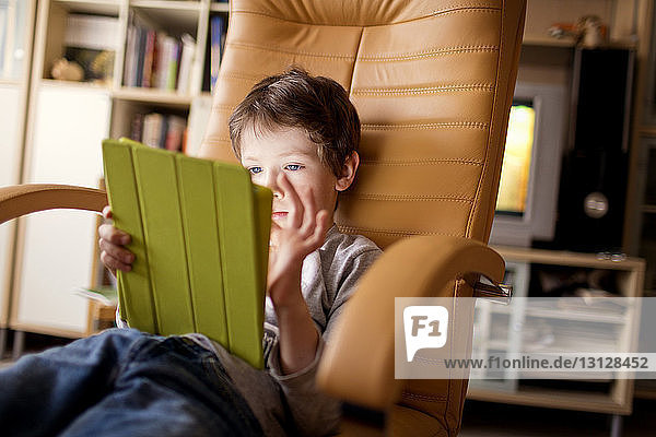 Junge benutzt Tablet-Computer  während er zu Hause auf einem Stuhl sitzt