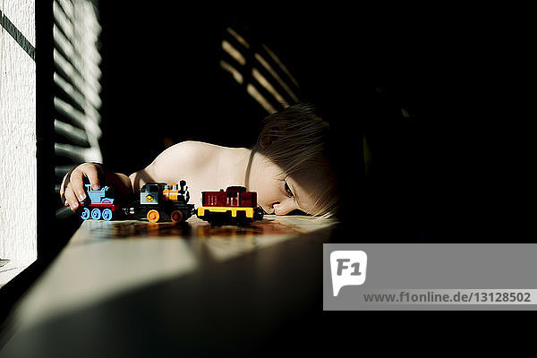 Boy playing with toy train while sitting at table by window