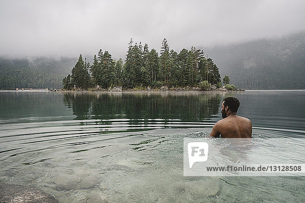 Rear view of shirtless man swimming in lake at forest