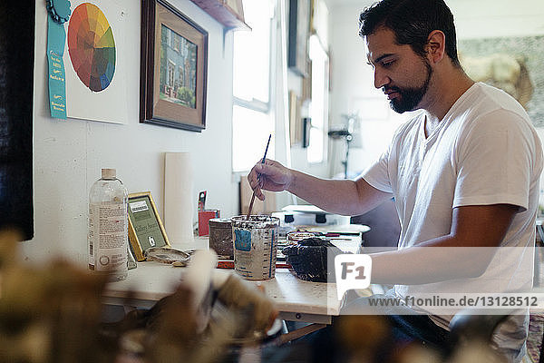 Side view of painter mixing colors in container at art studio