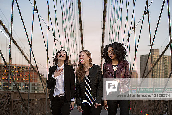Fröhliche Freunde gehen auf der Brooklyn Bridge bei klarem Himmel