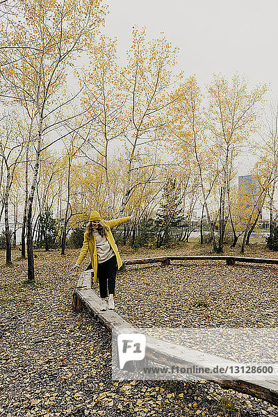 Playful woman walking on wooden benches at park during autumn