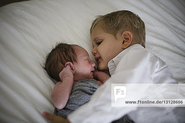 High angle view of boy lying by newborn brother on bed at home